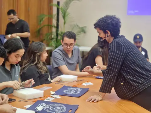 Estudiantes practican suturas en una mesa de trabajo mientras un instructor los observa