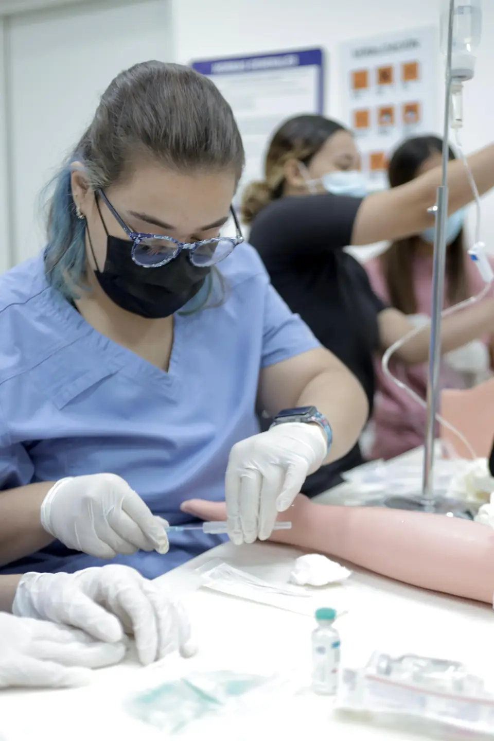 Participante con guantes canaliza una vía venosa en un brazo de simulación