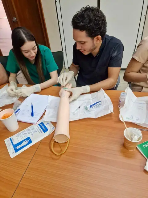 Estudiante practica la canalización venosa en un brazo de simulación junto a un instructor