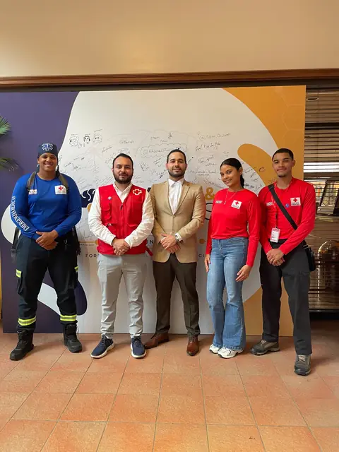 Equipo de la Cruz Roja Dominicana y de AFMEC frente al mural de firmas del evento